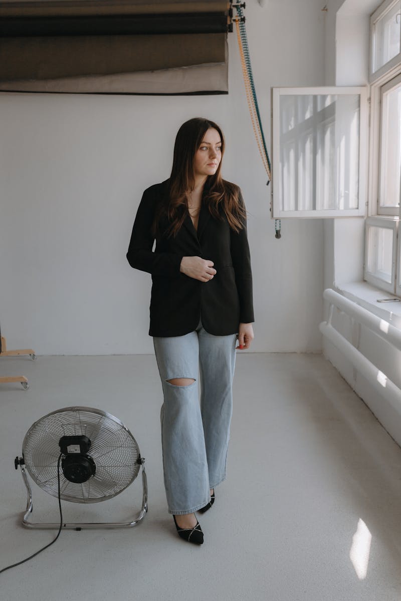 A woman in a black blazer and jeans standing in front of a fan